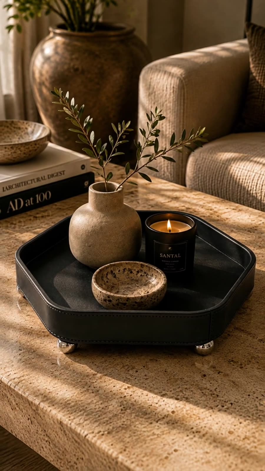 Black hexagonal tray on a console holding a candle, beside a vase and books